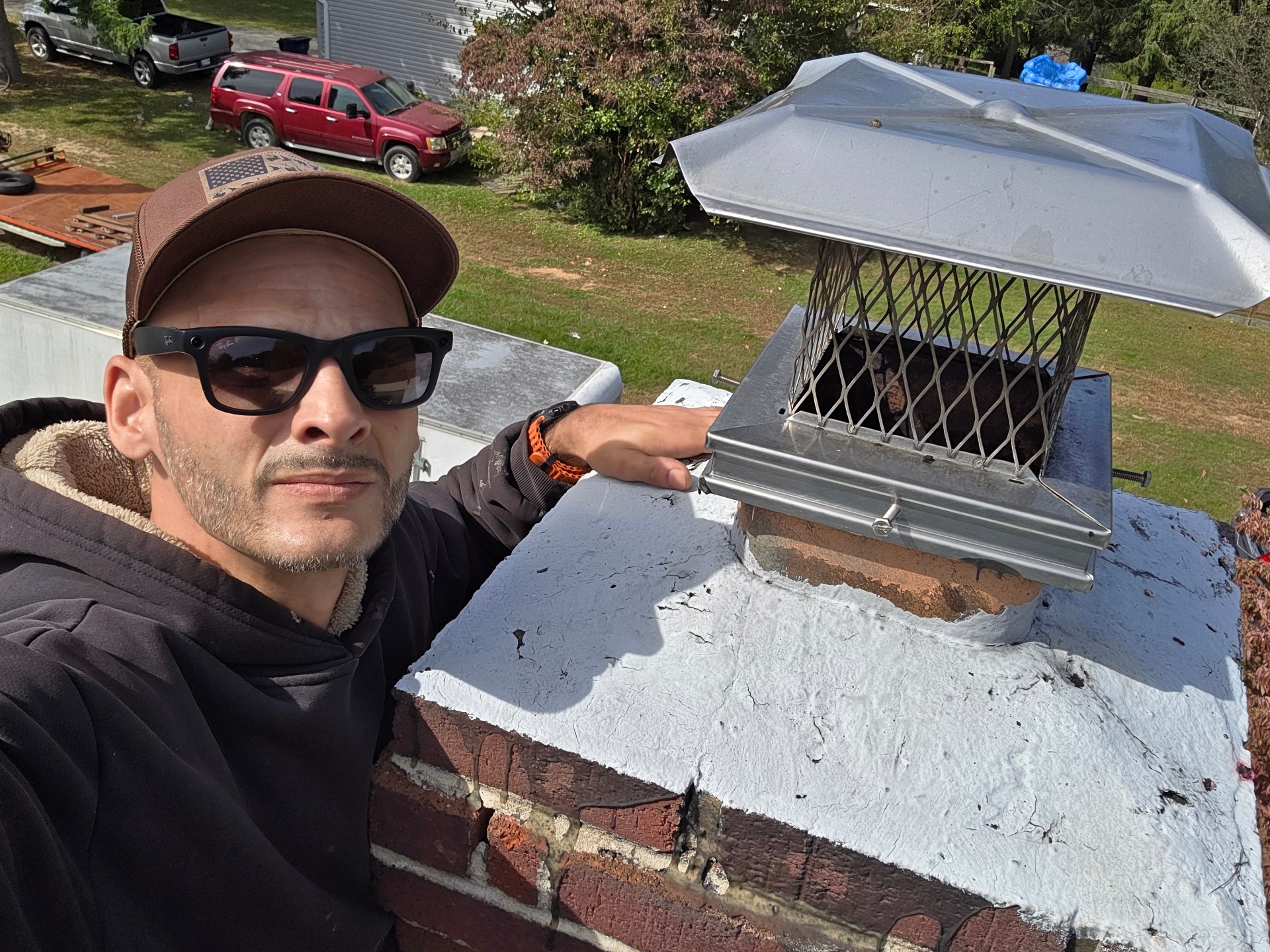 Chimney sweep beside a metal chimney cap on a brick chimney