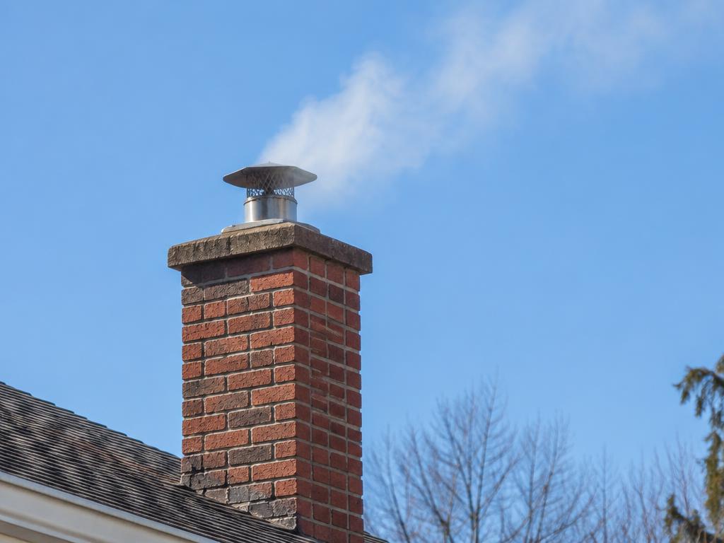 Thin smoke drifting from a chimney cap into a blue sky